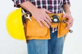 A handyman wearing a flannel, blue jeans, and his tool belt.