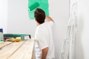 This is a picture of a painter painting a wall with a roller in light green paint.